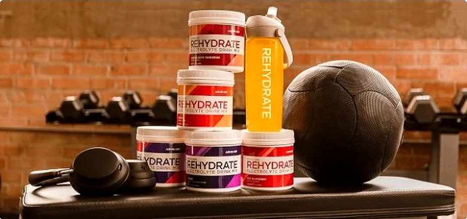 AdvoCare Rehydrate canisters in a gym setting with weights, water bottle, and headphones